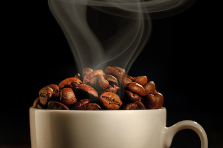 Steaming cup of coffee with coffee beans
